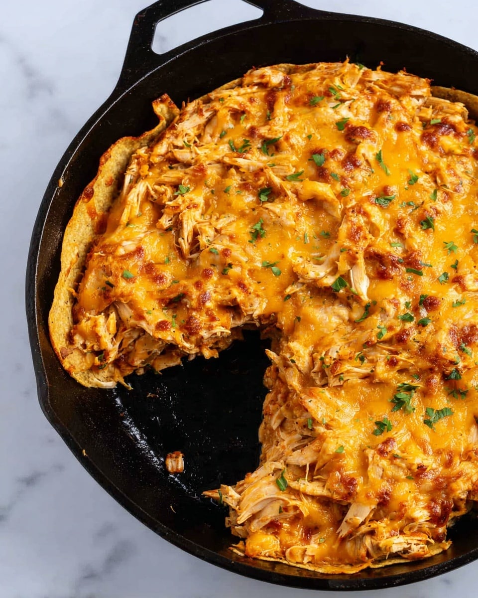 The image shows a black cast iron skillet with a cheesy chicken casserole inside, placed on a white marbled surface. The casserole has a single visible layer of shredded cooked chicken mixed with melted orange-yellow cheese and small bits of green herbs scattered over the top. The texture is slightly bubbly and browned in parts, with some chicken pieces showing a light golden color. A wedge has been cut out from the casserole, revealing a thin, crispy-looking tortilla layer on the left side, which is a pale golden color. The skillet itself has a slightly rough texture with some shiny spots where the light hits it. Photo taken with an iphone --ar 4:5 --v 7