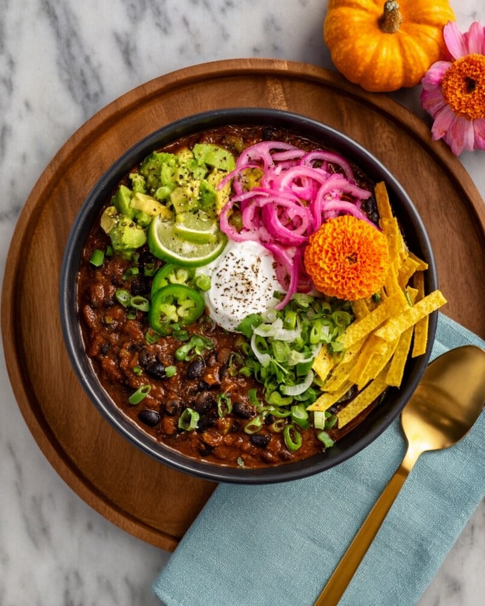 A round metal pot filled with thick chili, showing a reddish-brown sauce mixed with dark beans, sits on a round wooden board with a small orange pumpkin on the right side and a black ladle below the pot. Around the pot, there are four white bowls: the top left bowl contains cut green lime wedges and chopped avocado with an orange flower in the middle, the top right bowl holds thin slices of pink and white onions, the bottom right bowl is filled with shredded yellow cheese, and the bottom left bowl contains chopped green onions and fresh cilantro leaves. A white folded napkin with pink and orange flowers on top is placed near the bottom left of the board, and three gold spoons lie above the pot. The whole setting is on a white marbled texture surface. photo taken with an iphone --ar 4:5 --v 7