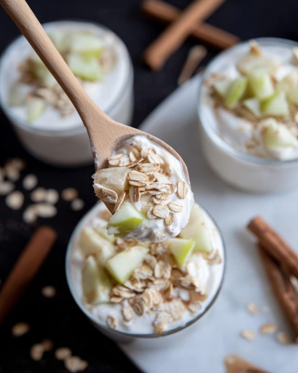 The image shows a close-up of a wooden spoon holding a scoop of yogurt topped with light beige oats and small pale green apple pieces. Below the spoon is a white bowl filled with a creamy white yogurt base, with more oats and apple pieces sprinkled on top. In the background, there are two more similar white bowls filled with the same layered mixture. The scene is set on a white marbled surface, scattered with some loose oats and a few cinnamon sticks, creating a cozy and fresh look. photo taken with an iphone --ar 4:5 --v 7