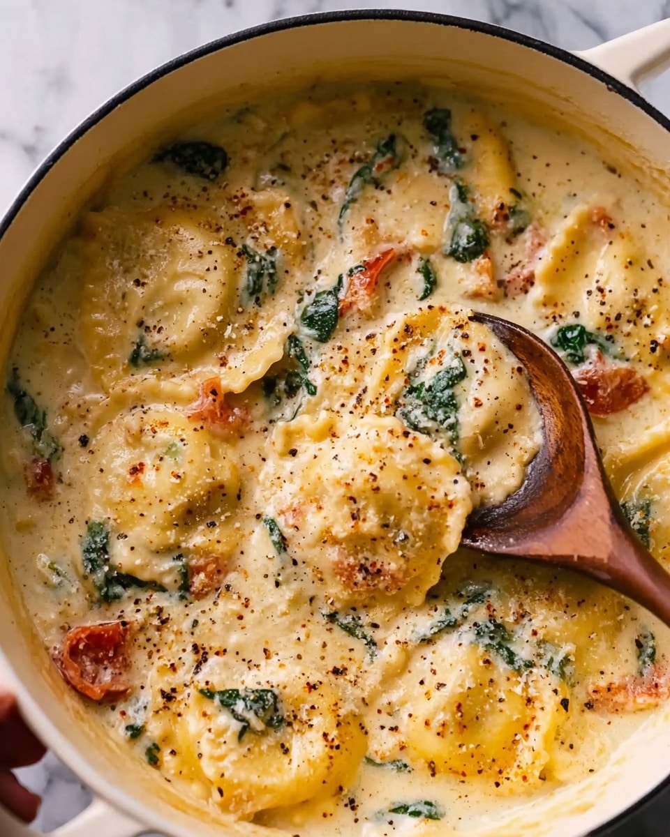 The image shows a close-up of ravioli pasta in a creamy sauce inside a white pot. The dish has several ravioli pieces with soft, flat edges and a yellowish color, coated in a thick, light cream sauce speckled with melted cheese. There are green spinach leaves mixed throughout, and small chunks of red tomato add color contrast. The dish is sprinkled with black pepper, making the surface look slightly textured. A wooden spoon is scooping some ravioli from the pot, held by a woman's hand. The background is a white marbled texture. Photo taken with an iphone --ar 4:5 --v 7