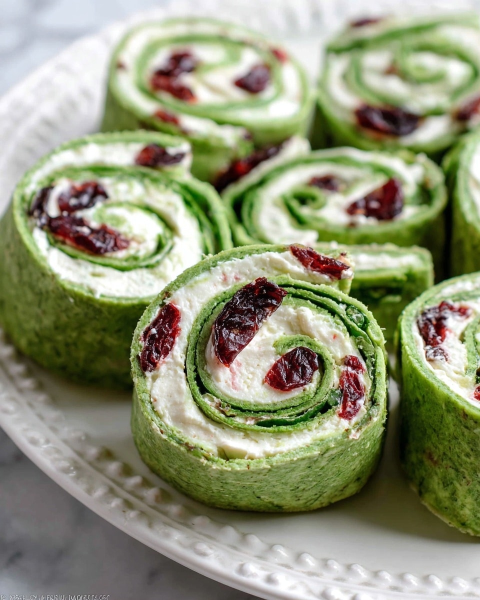 The image shows several green wraps cut into thick pinwheel slices, arranged closely on a white plate with a detailed edge. Each wrap has three visible layers: a bright green outer spinach tortilla with a soft texture, a middle layer of creamy white cheese, and scattered deep red dried cranberries embedded in the cheese. The spirals formed by the green tortilla and white cheese give a sense of depth and softness. The background is a white marbled texture. photo taken with an iphone --ar 4:5 --v 7