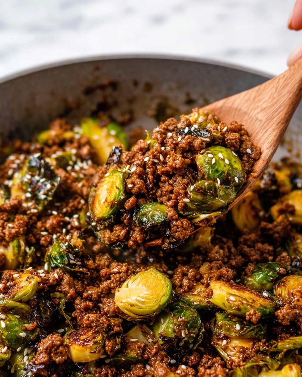 The image shows a close-up of cooked ground beef mixed with roasted Brussels sprouts, both having a rich brown and golden color with some charred edges. The ground beef appears crumbly and juicy, cooking evenly with a glossy, slightly oily texture that coats the Brussels sprouts. The Brussels sprouts are halved, with their green and light yellow layers visible, some leaves appearing wilted and crispy. White sesame seeds are sprinkled on top, adding small white dots contrasting with the darker colors of the meat and vegetables. A wooden spoon is scooping a portion of the mixture, with a woman's hand slightly visible holding the spoon from the left side, and the whole scene sits on a white marbled background. photo taken with an iphone --ar 4:5 --v 7