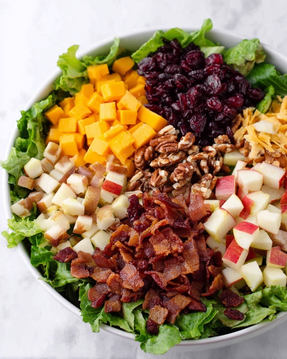 A large white bowl with a layer of green chopped lettuce at the bottom is topped with five distinct sections: bright yellow cheese cubes on the left, dark red dried cranberries below the cheese, crispy reddish-brown bacon pieces on the bottom right, white and red-skinned chopped pear pieces above the bacon, and roughly chopped brown pecans at the top. The bowl is placed on a white marbled texture with scattered dried cranberries around it. A small glass jar with a creamy light brown dressing sits at the top left corner, with some drops of dressing and dried cranberries nearby. A pink and white checkered cloth and silver forks are visible at the top right corner. photo taken with an iphone --ar 4:5 --v 7