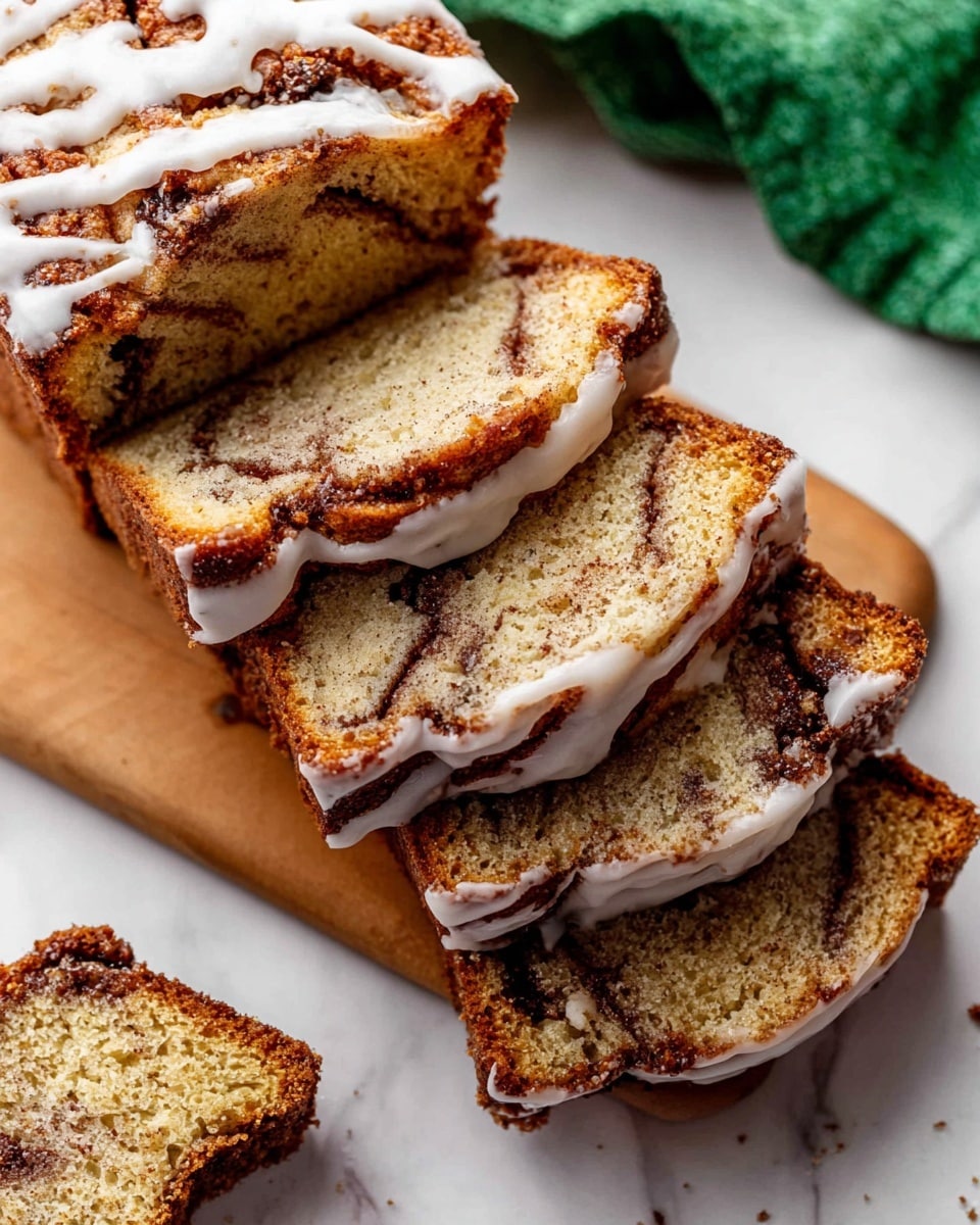 A rectangular banana bread loaf sits on a dark wooden cooling rack placed over a white marbled surface. The top of the bread has a golden-brown crust with swirls of light brown cinnamon mixed with the soft texture of the bread. There are three banana slices embedded in the top layer, visible through a glaze of creamy white icing that is unevenly spread, creating a drizzled effect over the cinnamon patterns. Around the cooling rack, three yellow bananas with brown spots lie on the white marbled surface, highlighting the main ingredient of the bread. photo taken with an iphone --ar 4:5 --v 7