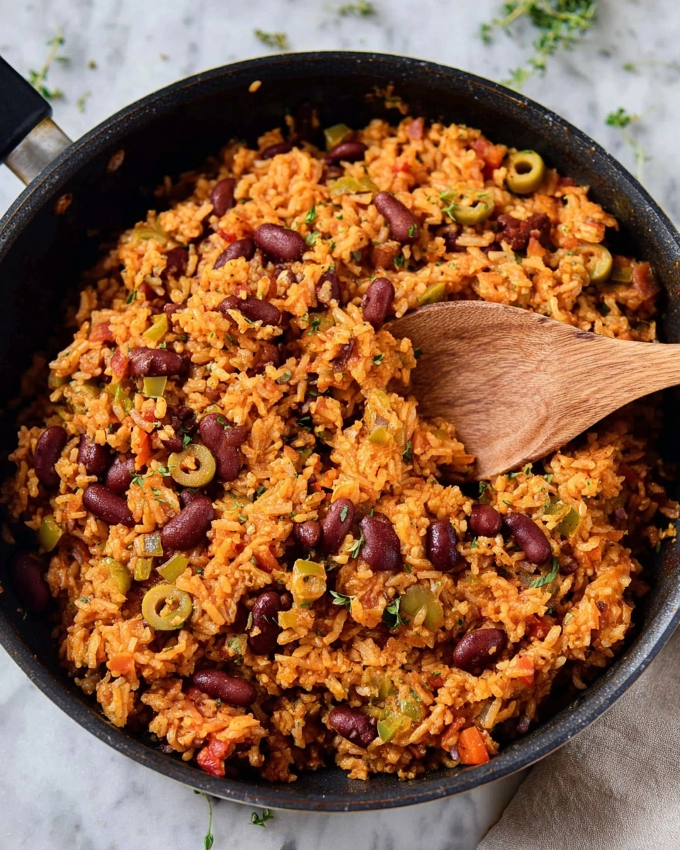 A close-up view of a black skillet filled with a cooked rice dish that has visible layers of orange-colored rice mixed with dark red kidney beans, chopped green olives, and small pieces of red and green vegetables. The rice looks moist and fluffy with a slightly oily texture. A wooden spoon is placed inside the skillet, partially stirring the rice and beans mix. The skillet is set on a white marbled surface with some scattered small green herbs around. Photo taken with an iphone --ar 4:5 --v 7