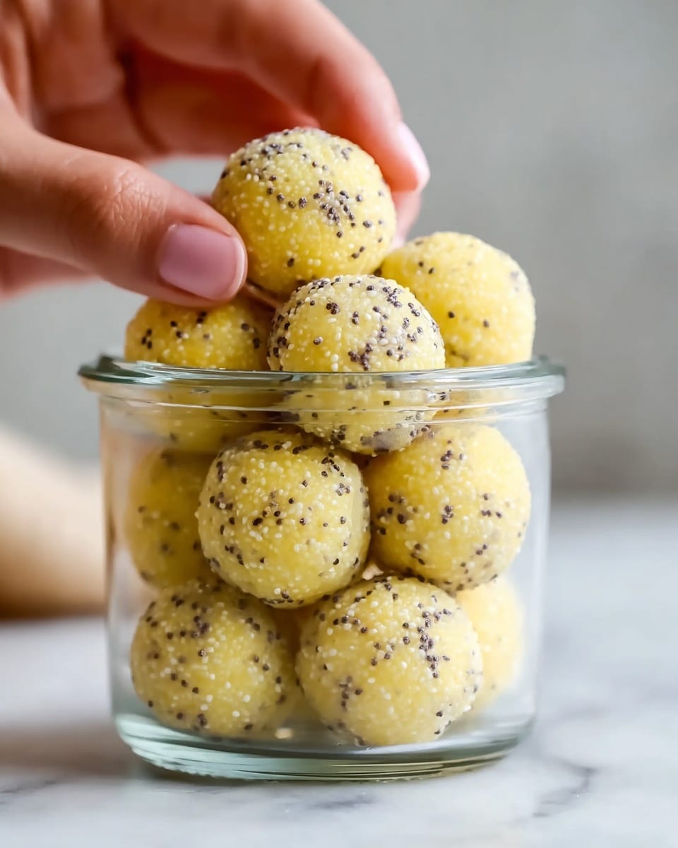 A clear glass jar is filled with round, light yellow balls that have small black and white seeds sprinkled all over them, giving a textured look. The balls are stacked in two full layers inside the jar, with one ball held gently by a woman's hand at the top, showing the smooth yet bumpy surface of the seeds. The jar sits on a white marbled surface, with soft lighting that highlights the pale yellow and seed details on the balls. The background is softly blurred, keeping the focus on the jar and the balls inside it. photo taken with an iphone --ar 4:5 --v 7