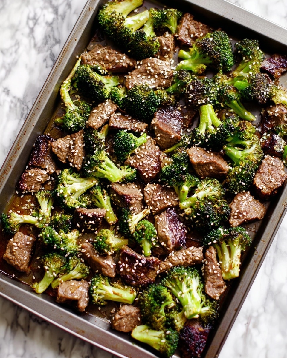 The image shows a baking tray filled with cooked beef pieces and broccoli florets. The beef is cut into bite-sized chunks with a brown, slightly crispy surface, while the broccoli is bright green with some charred edges. Both ingredients are scattered evenly across the tray, topped with small white sesame seeds that add texture. The tray rests on a white marbled surface, enhancing the vibrant colors of the food. photo taken with an iphone --ar 4:5 --v 7