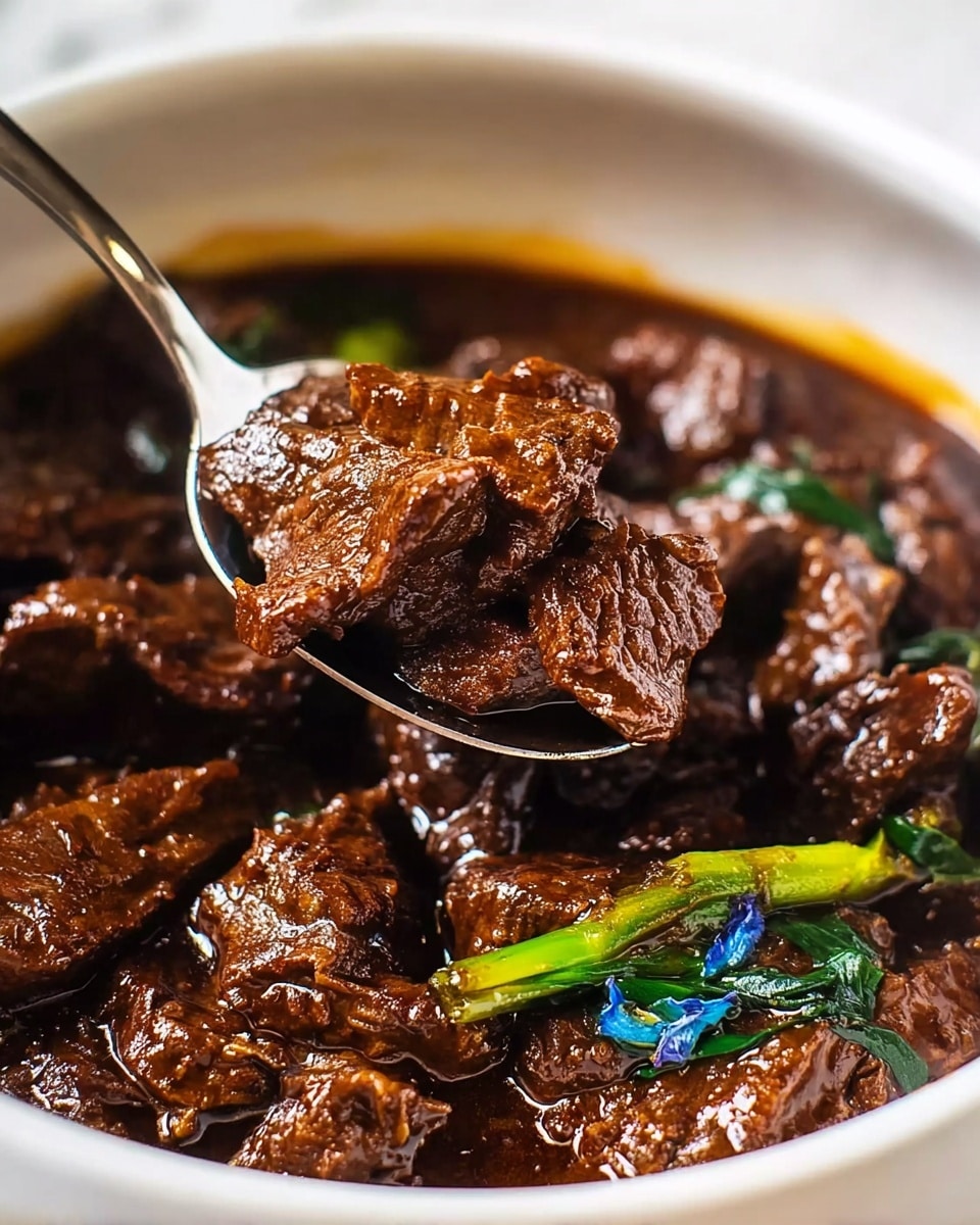 A close-up view of a dish of dark brown, tender beef slices cooked in a rich, glossy sauce inside a white bowl. The sauce has a thick texture, clinging to the meat, and shows some small bits of green vegetables with hints of blue flowers scattered throughout. A shiny metal spoon lifts a portion of the beef, highlighting the juicy, well-coated texture of the meat. The bowl rests on a white marbled surface. photo taken with an iphone --ar 4:5 --v 7