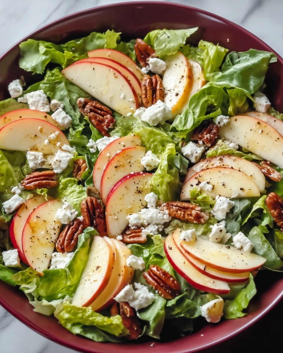 A white bowl is filled with fresh green lettuce leaves as the base layer, topped with evenly spread thin slices of red apple with white flesh. Scattered between the apple slices are small chunks of white feta cheese with a crumbly texture. Among these layers, there are medium brown pecan halves adding a crunchy element. The whole salad is lightly sprinkled with black pepper. The bowl sits on a white marbled textured surface. photo taken with an iphone --ar 4:5 --v 7
