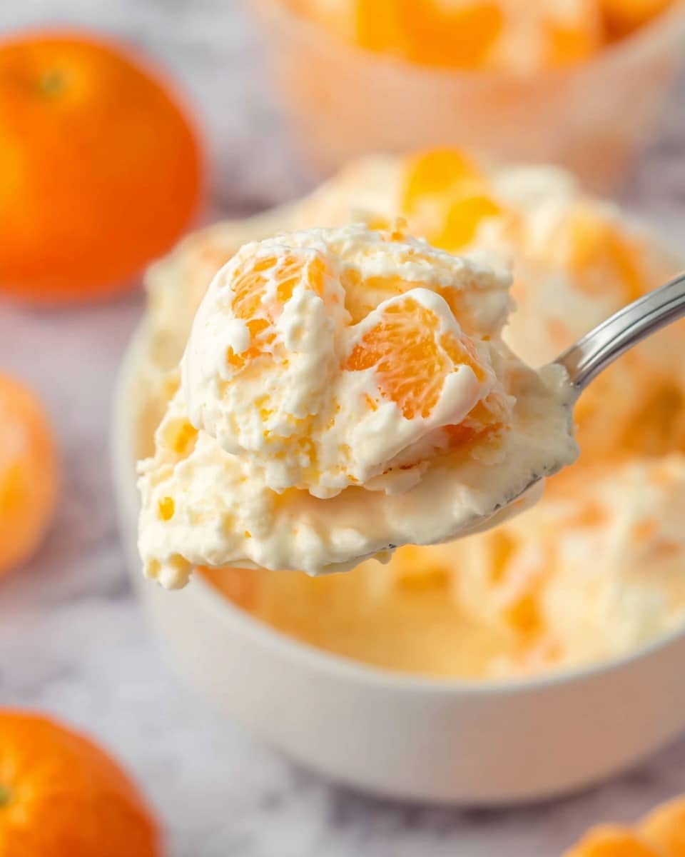 A white bowl is filled with a creamy, light orange dip that has visible pieces of bright orange mandarin segments and small white mini marshmallows mixed throughout. Around the bowl, on a white marbled surface, are loose mini marshmallows scattered, a smaller white bowl filled with mandarin segments in the top left, triangular pieces of pineapple on the bottom left, several whole mandarins placed near a white cloth with a blue check pattern on the right, and a small round wooden bowl full of more mini marshmallows at the bottom right. The dip looks thick and textured with the fruit and marshmallow pieces clearly visible photo taken with an iphone --ar 4:5 --v 7