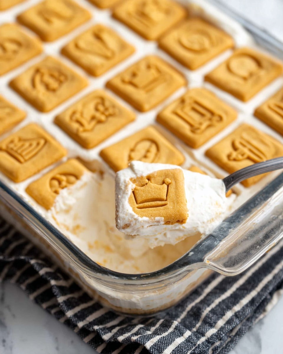 A slice of layered dessert on a white plate, showing three main layers: a bottom layer of square vanilla cookies that are light tan with a slightly crisp texture, a middle layer of light yellow banana slices, and a thick top layer of creamy white filling with a soft and airy texture; the dessert is topped with two square vanilla cookies with a light golden pattern, one of which has a bite taken out of it, revealing the soft filling inside. The plate sits on a white marbled surface with blurred bananas and a glass of milk in the background. photo taken with an iphone --ar 4:5 --v 7