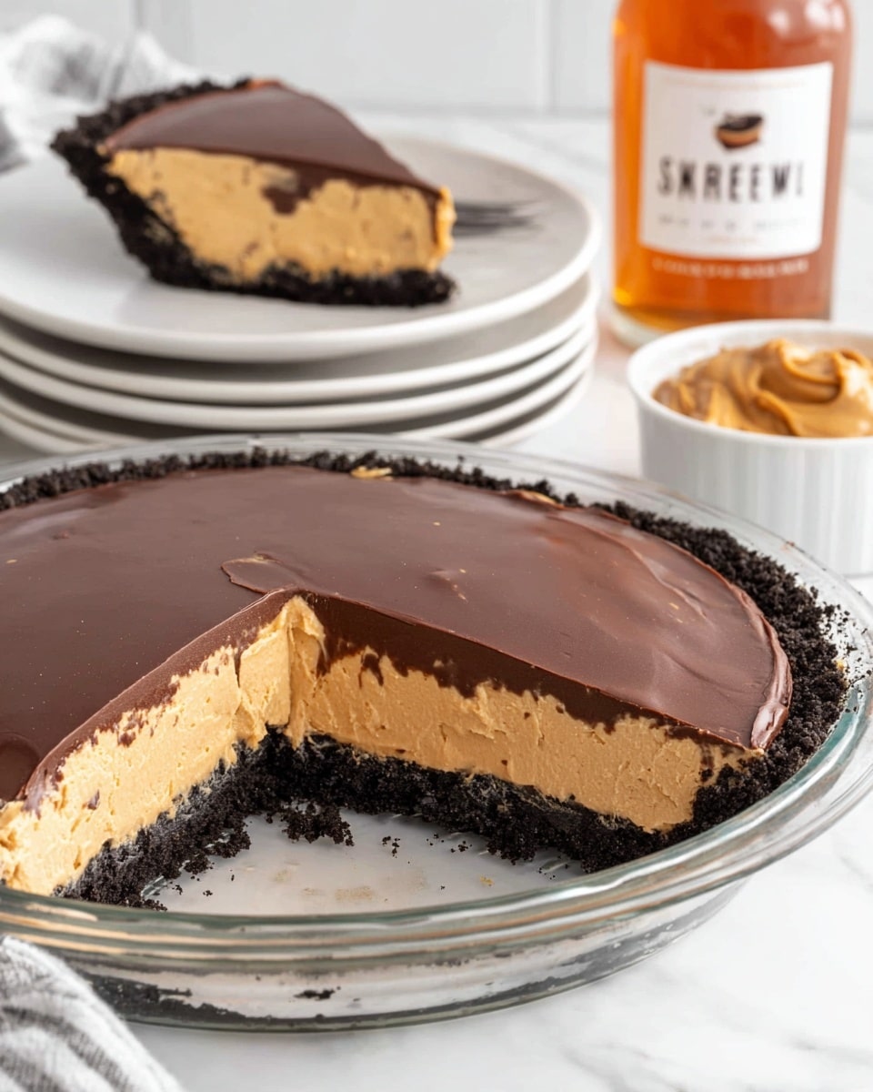 A glass pie dish holds a three-layer peanut butter pie with a dark crumb crust at the bottom, a thick creamy peanut butter middle layer in tan color, and a smooth dark chocolate layer on top. A slice is cut out from the pie and placed on a stack of white plates in the background. Next to the pie dish is a small white bowl filled with peanut butter and a bottle with an orange-brown liquid and a white label. The whole scene is set on a white marbled surface. Photo taken with an iphone --ar 4:5 --v 7