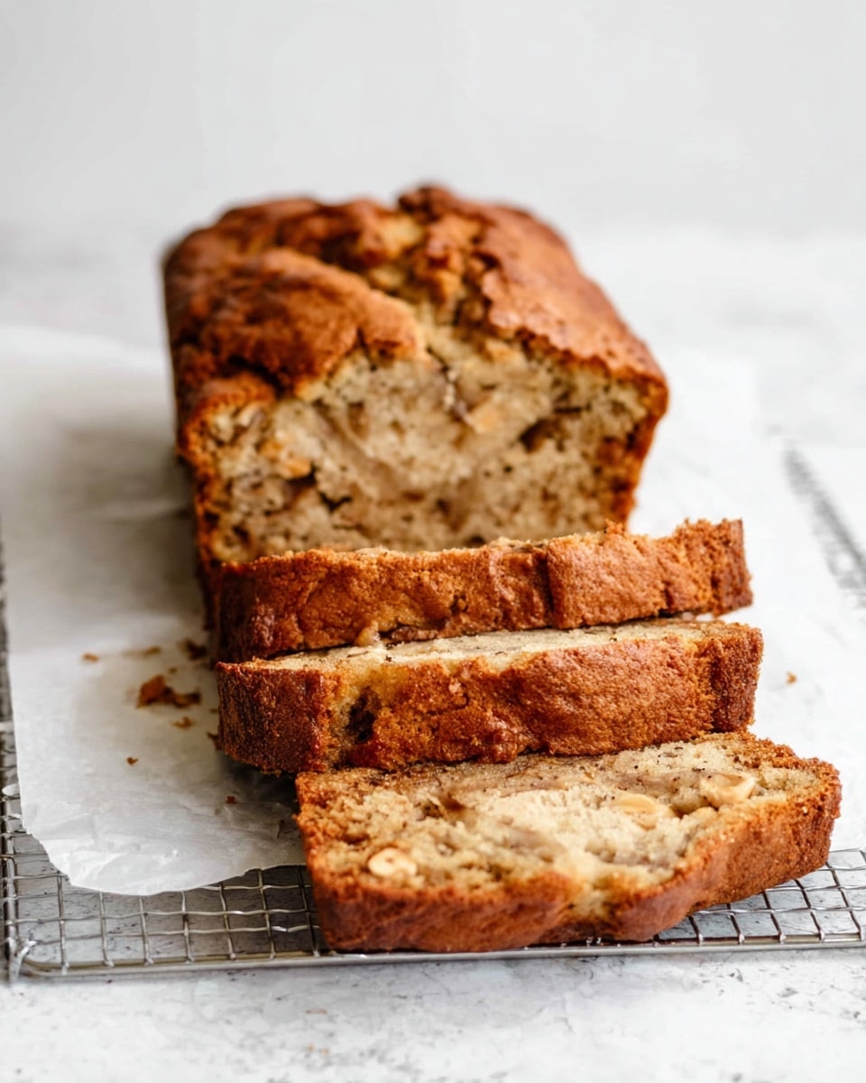 The image shows a loaf of banana bread with a crusty, golden-brown top and sides, slightly cracked on top. The bread has been sliced, showing a soft, light brown inside dotted with darker spots of banana and nuts. Three slices lie flat in front of the remaining loaf, all resting on white parchment paper over a metal cooling rack, set on a white marbled textured surface. The texture of the bread looks moist and dense with visible bits of nuts. Photo taken with an iphone --ar 4:5 --v 7