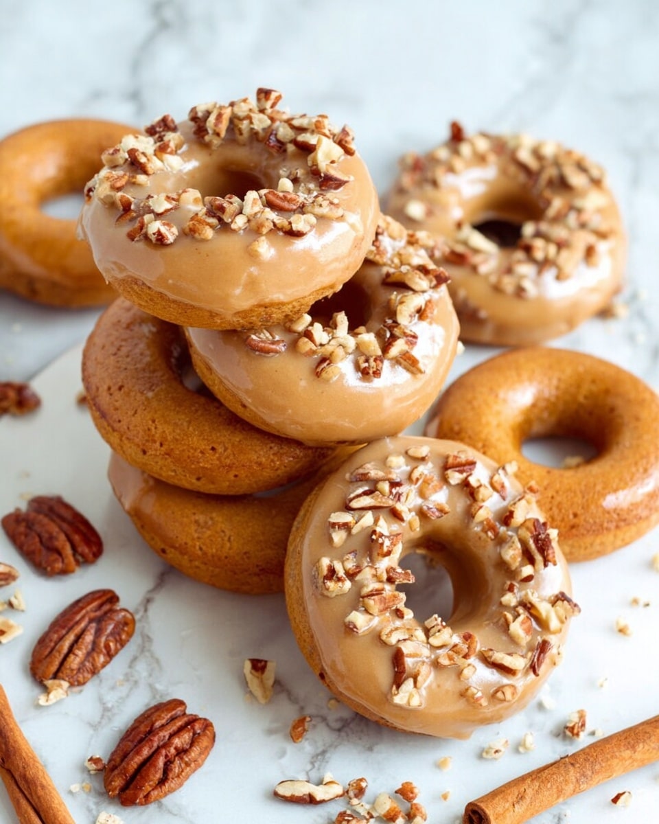 A pile of seven glazed doughnuts sits on a white marbled surface, arranged in a loose stack with some doughnuts partly overlapping others. Each doughnut has a shiny light brown caramel glaze coating the top, dotted with small pieces of chopped pecans that add texture and contrast. The dough underneath is a warm golden brown with a soft, slightly porous texture. Around the doughnuts, whole pecans and a few cinnamon sticks are scattered, adding to the rustic feel. The background is a white marbled texture with a soft cloth in one corner, creating a cozy and fresh look. photo taken with an iphone --ar 4:5 --v 7