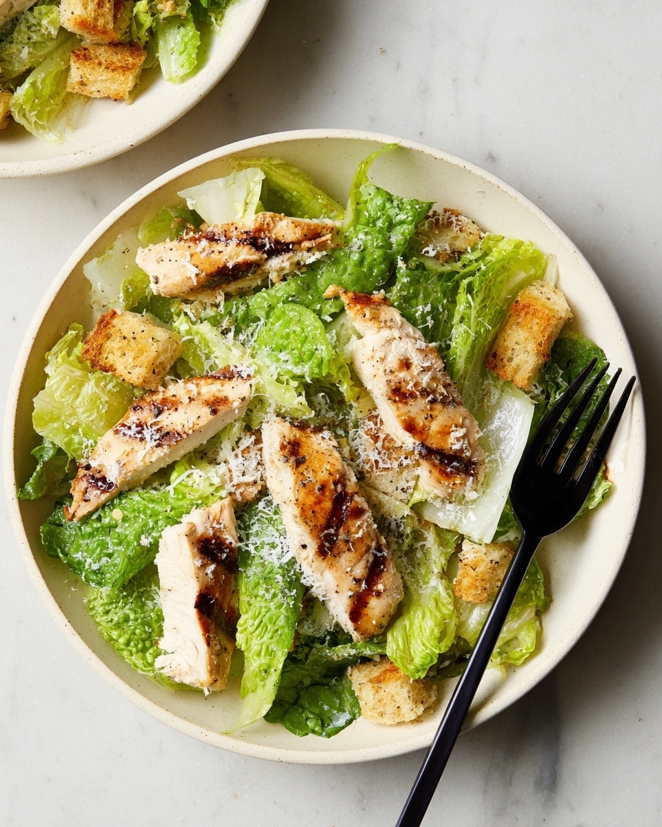 A white round plate holds a simple salad with bright green romaine lettuce leaves as the bottom layer, showing a crisp and fresh texture. On top, there are several slices of grilled chicken breast, marked with dark grill spots and a light golden brown color. Scattered among the lettuce and chicken pieces are small, crunchy croutons that are golden and slightly toasted. The salad is lightly sprinkled with finely grated white cheese, adding a soft texture all over. A black fork rests on the right side of the plate, placed on a white marbled surface. photo taken with an iphone --ar 4:5 --v 7