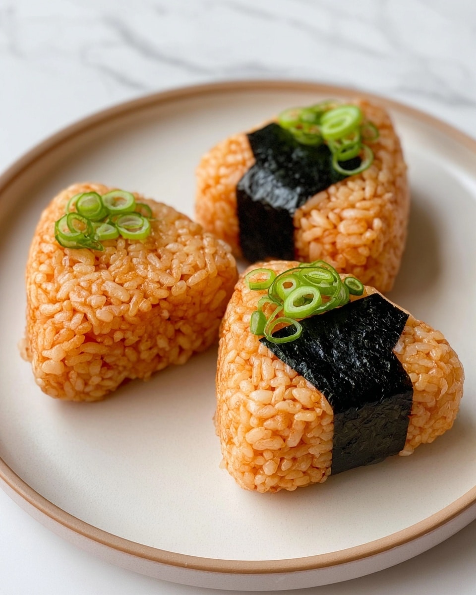Three triangular rice balls are placed on a white plate with a subtle beige rim, set against a white marbled texture. Each rice ball is made from tightly packed, orange-colored rice, showing a slightly glossy texture indicating moisture. In the middle of each rice ball is a dark, smooth rectangular strip of seaweed wrapped around it horizontally. The top corners of two rice balls are decorated with fresh, thinly sliced green onions, adding a bright green contrast to the orange rice. The rice grains are clearly visible, giving a textured and soft look to the rice balls. photo taken with an iphone --ar 4:5 --v 7